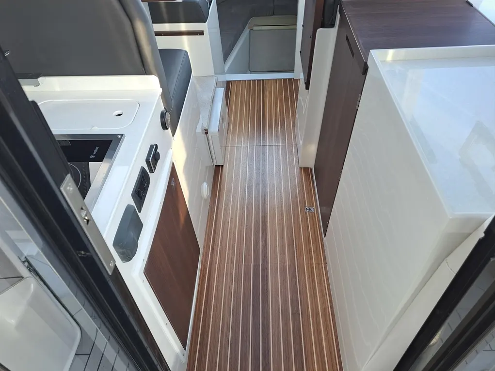 Interior of a boat showing a sleek wooden floor, kitchenette with a hob and storage, creating a modern aesthetic.